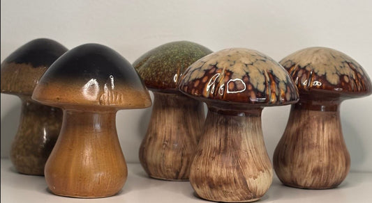 Row of ceramic mushrooms with different colored caps on a plain background