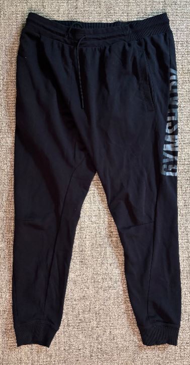 Black jogger pants with a brand logo on the side, laid flat on a textured surface.