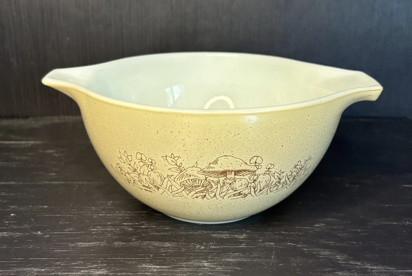 Beige ceramic mixing bowl with floral pattern on a dark surface