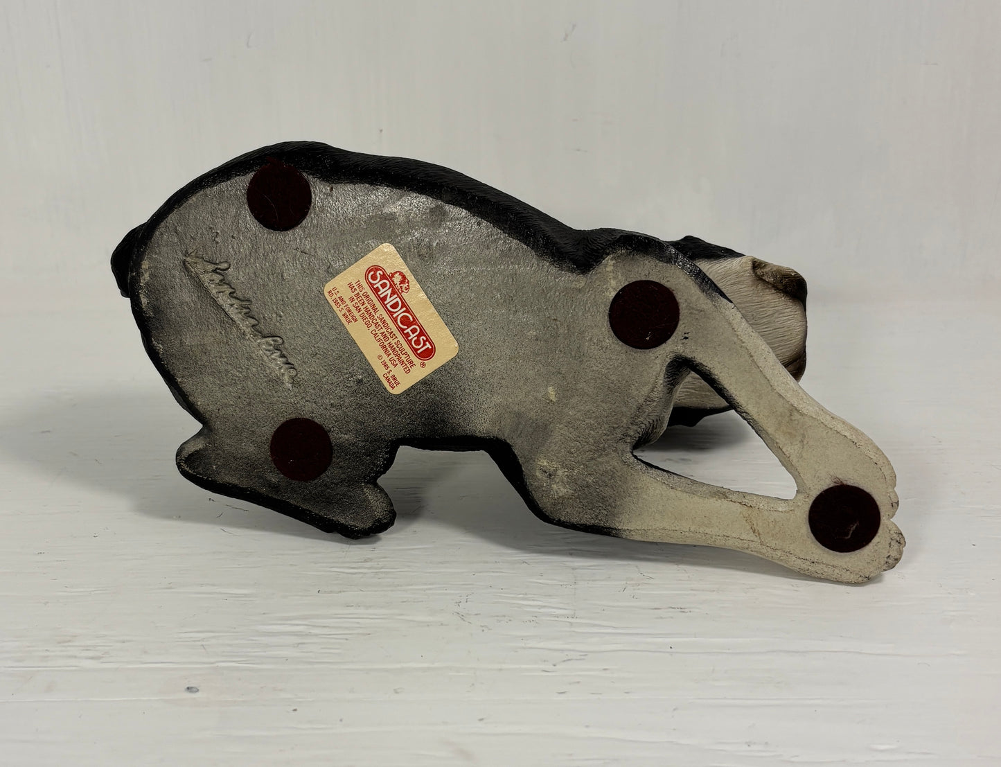 Vintage cast iron dog-shaped door stop with a label on a white background