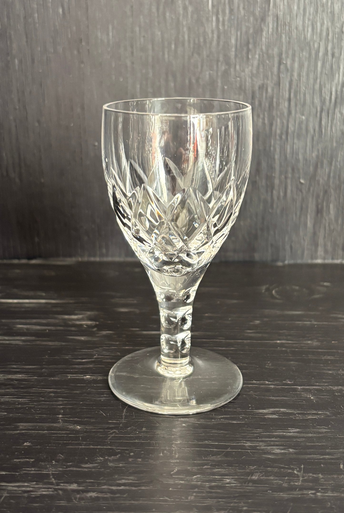 Clear glass wine glass with cut patterns on a dark wooden surface
