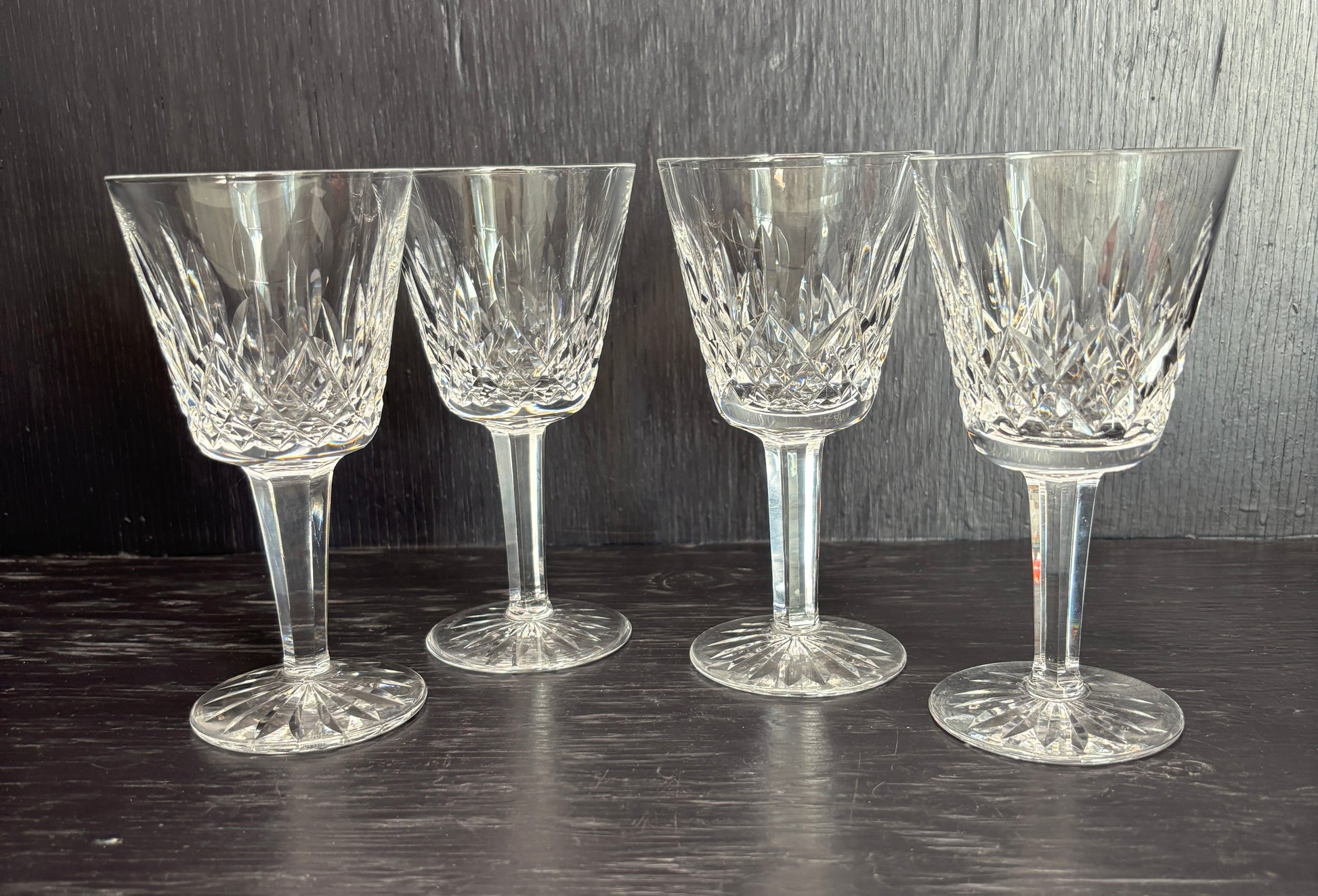 Four crystal wine glasses on a dark surface with a dark background