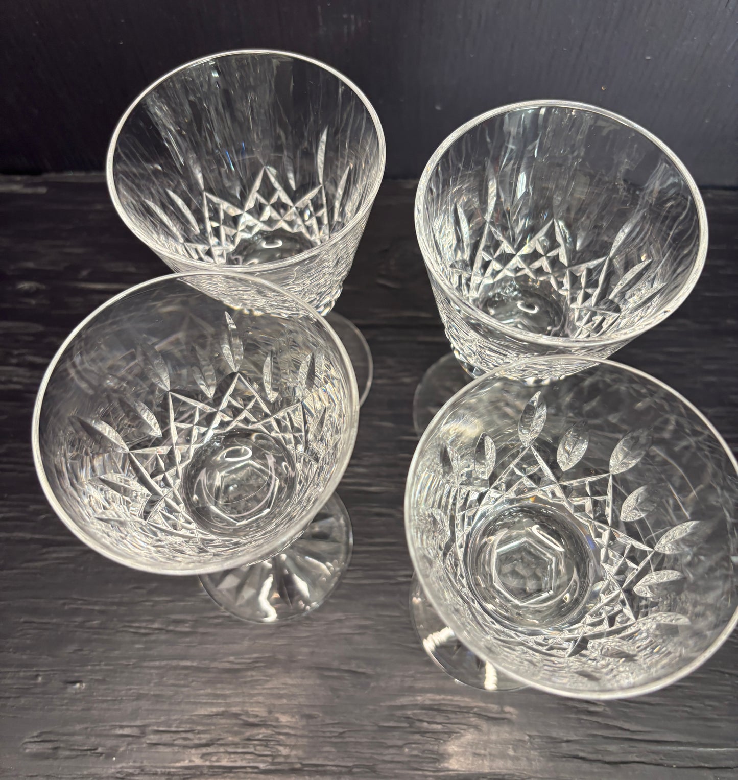 Four crystal glasses with engraved designs on a dark wooden surface