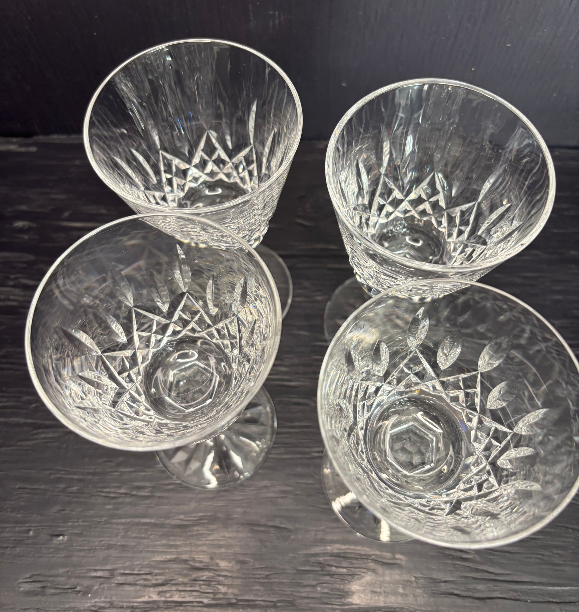 Four crystal glasses with engraved designs on a dark wooden surface