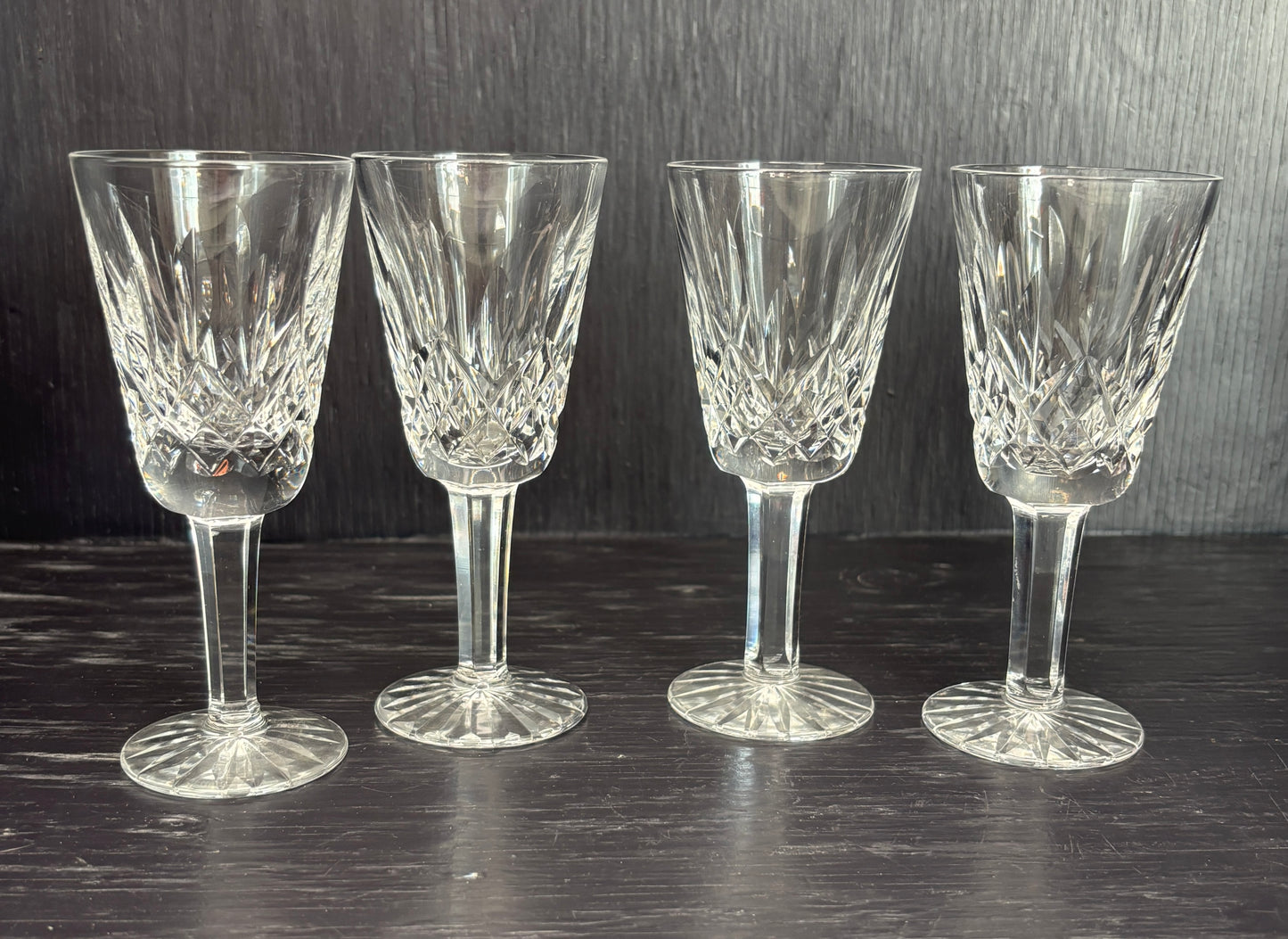 Four crystal sherry glasses on a dark surface with a dark background