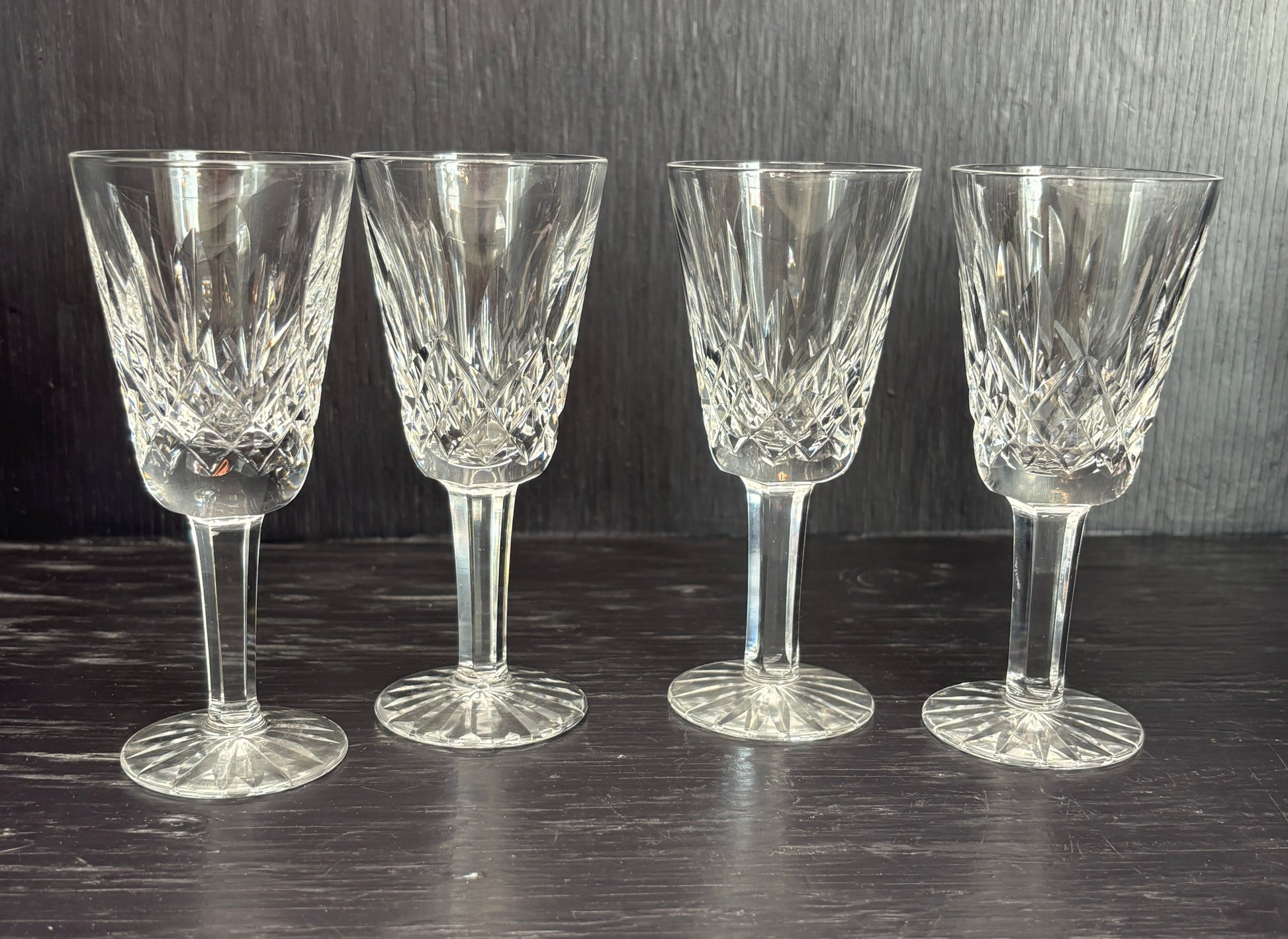 Four crystal sherry glasses on a dark surface with a dark background