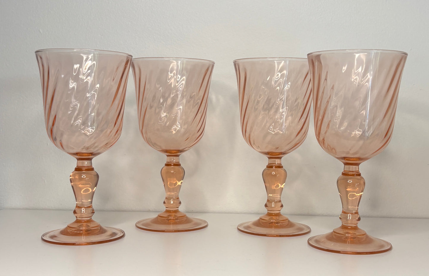Four pinkish-brown glass goblets on a white surface with a light gray background