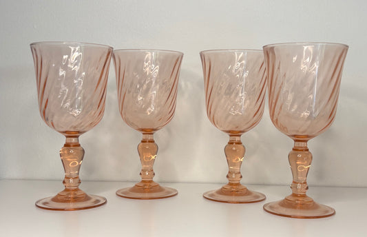 Four pinkish-brown glass goblets on a white surface with a light gray background