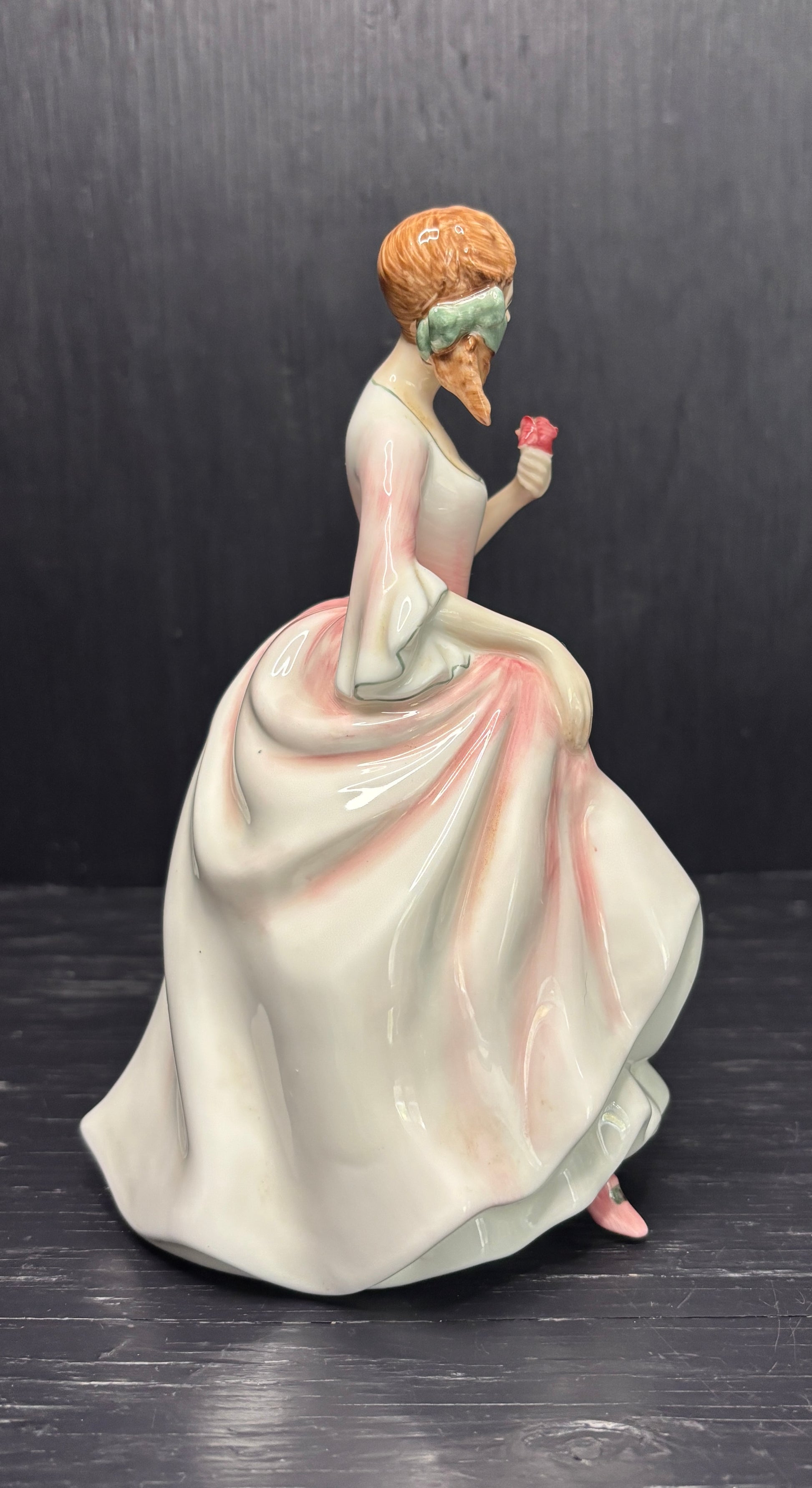 Figurine of a woman in a white dress holding a flower against a dark background