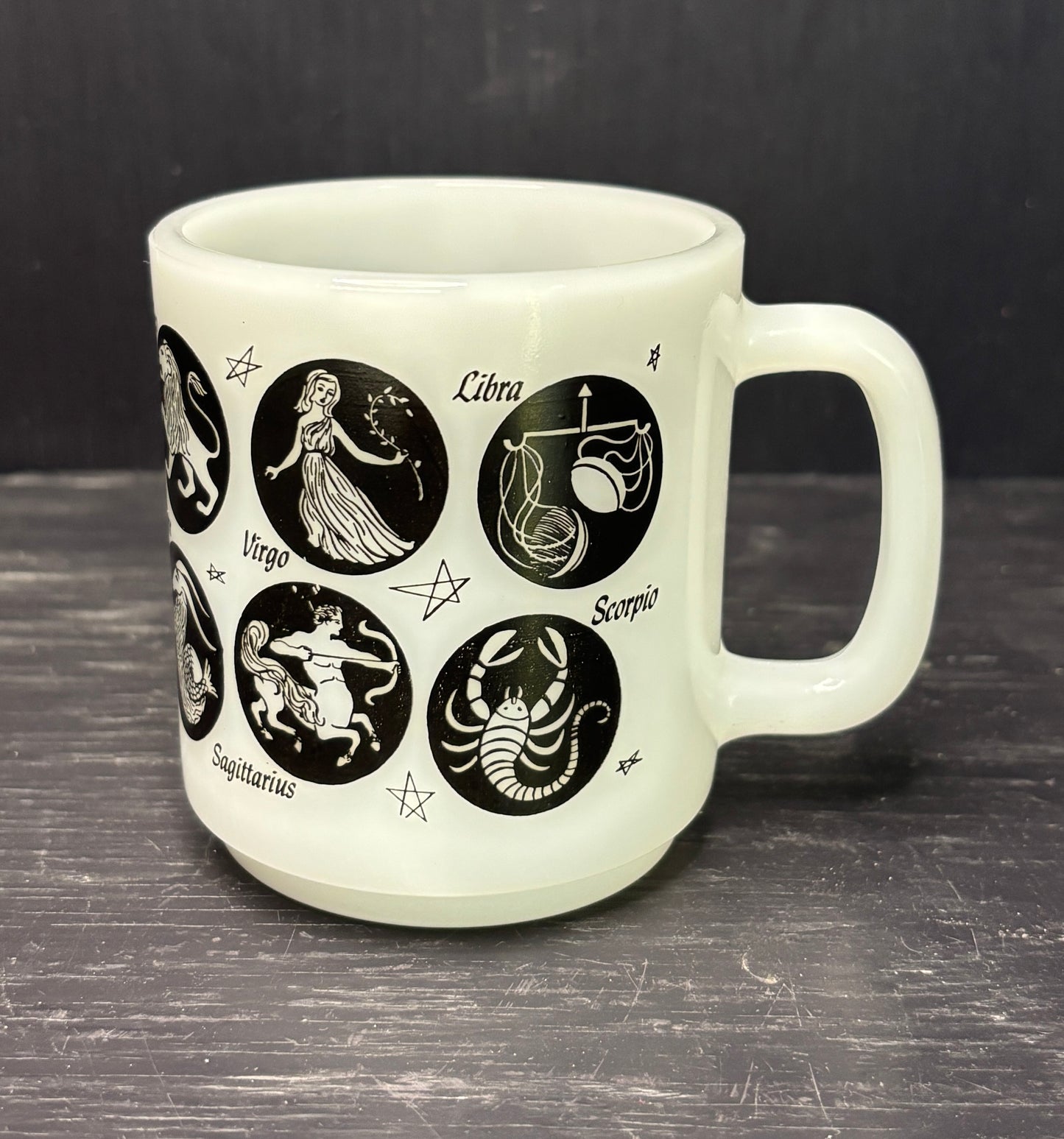 White mug with black zodiac illustrations on a dark surface