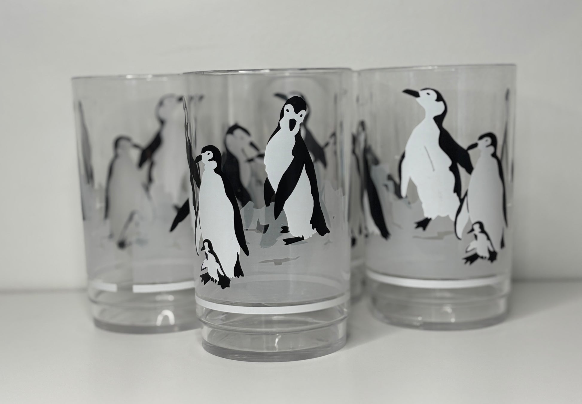 Three glass tumblers with penguin designs on a white background