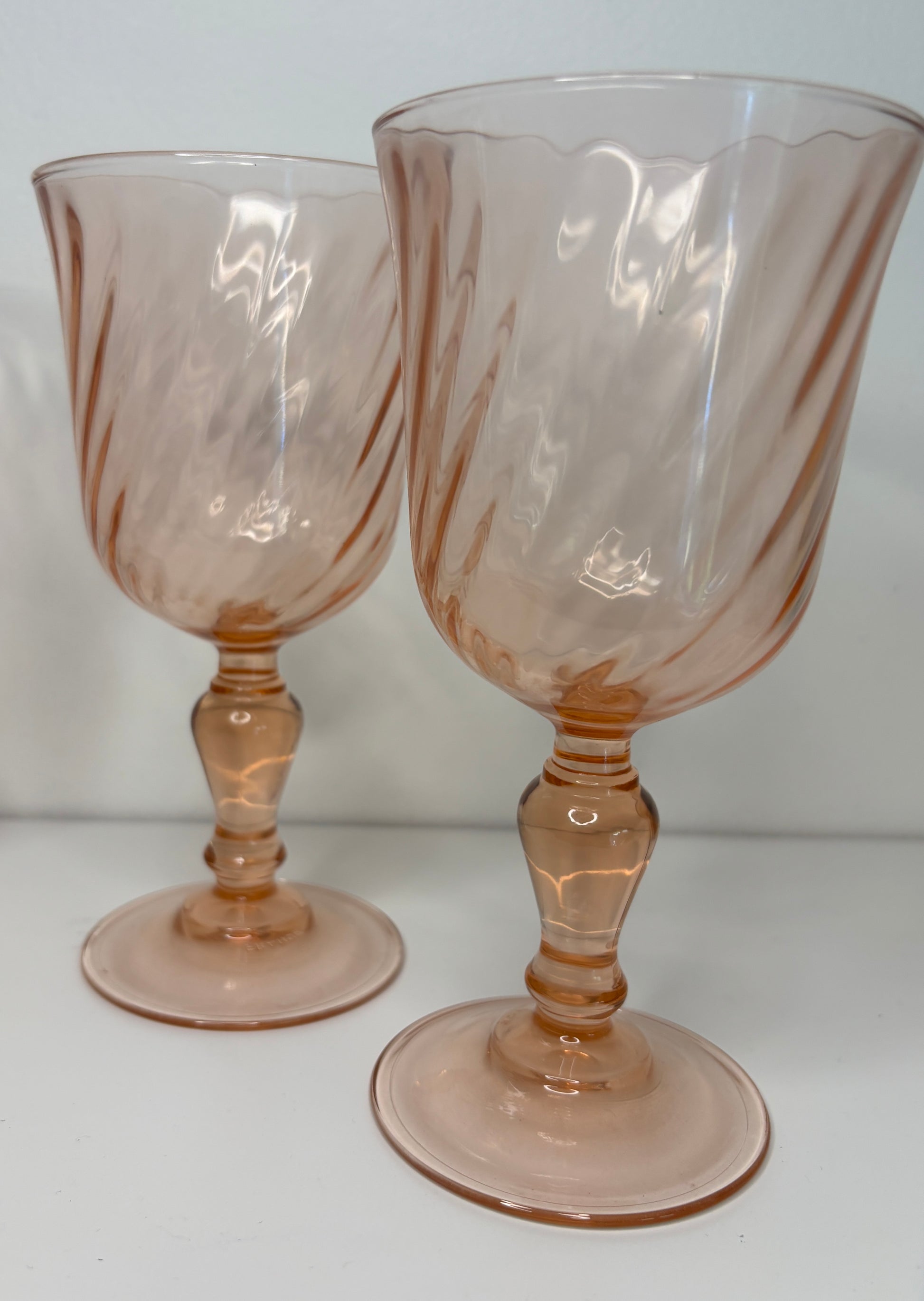 Two pink glass goblets with decorative stems on a white background