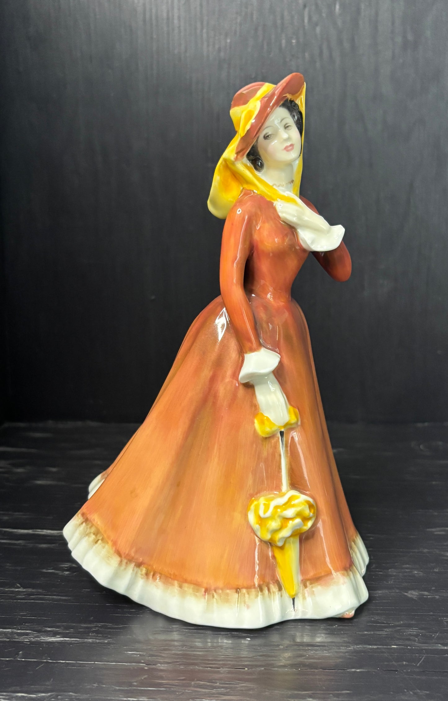 Vintage ceramic figurine of a woman in a long dress and bonnet on a dark background