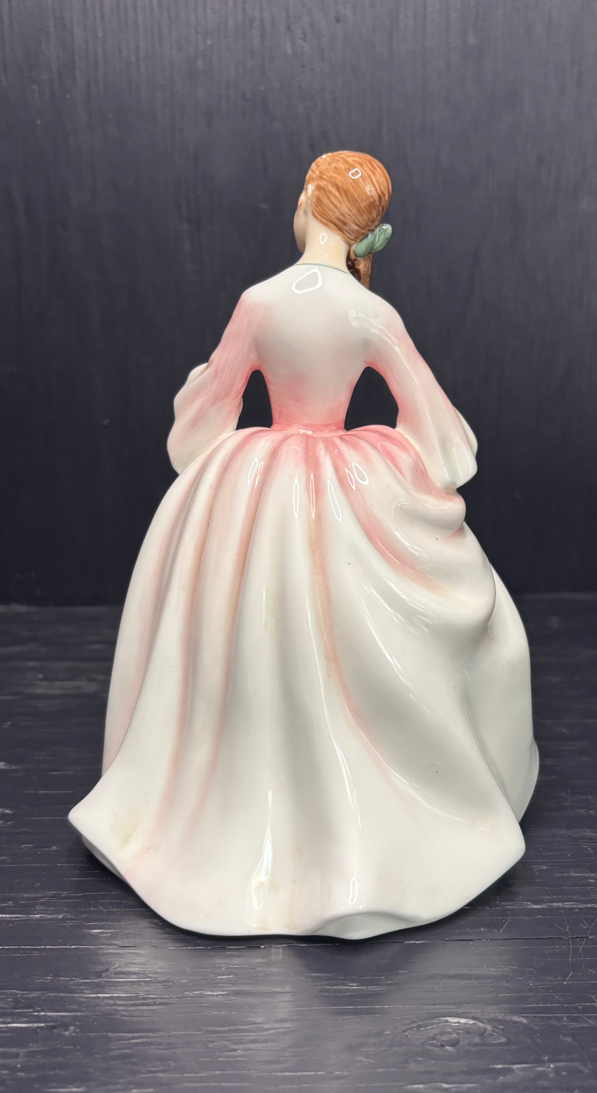 Porcelain figurine of a woman in a white dress with pink accents on a dark background