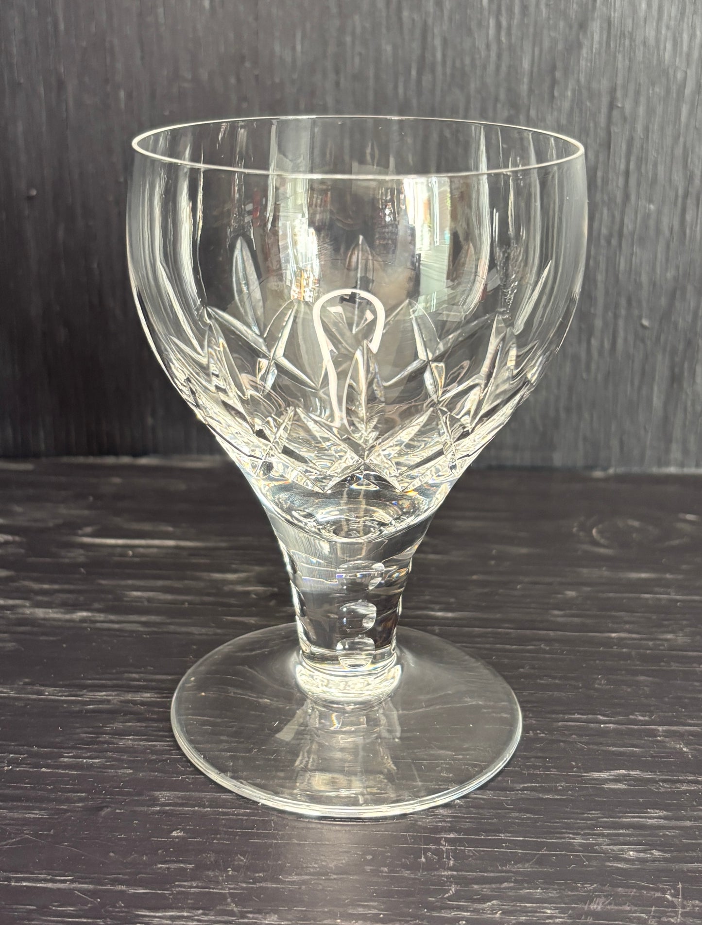 Clear glass goblet with intricate cut design on a dark wooden surface