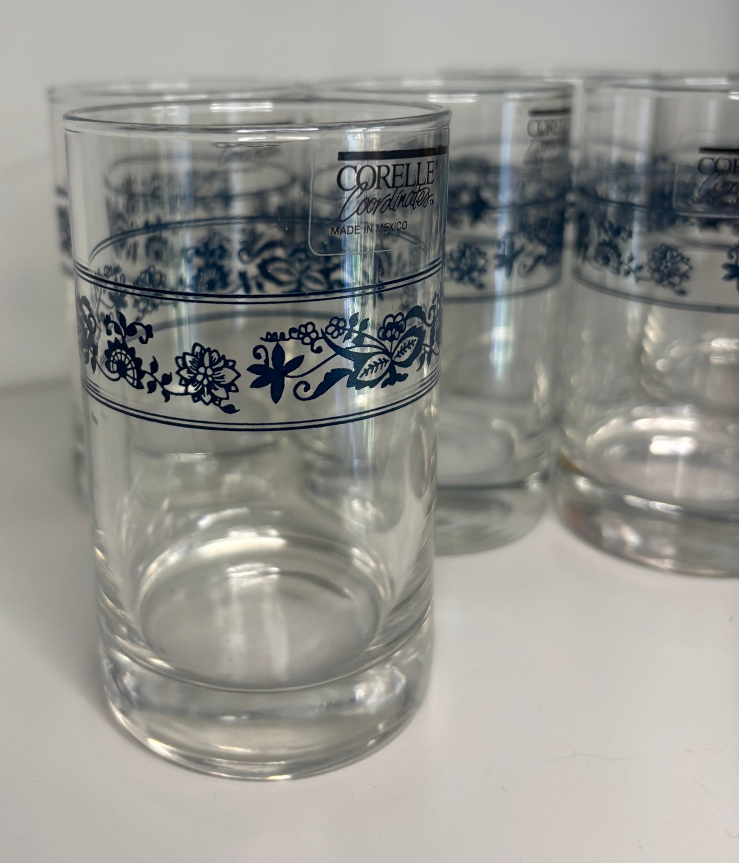 Clear glasses with blue floral patterns and Corelle branding on a white background