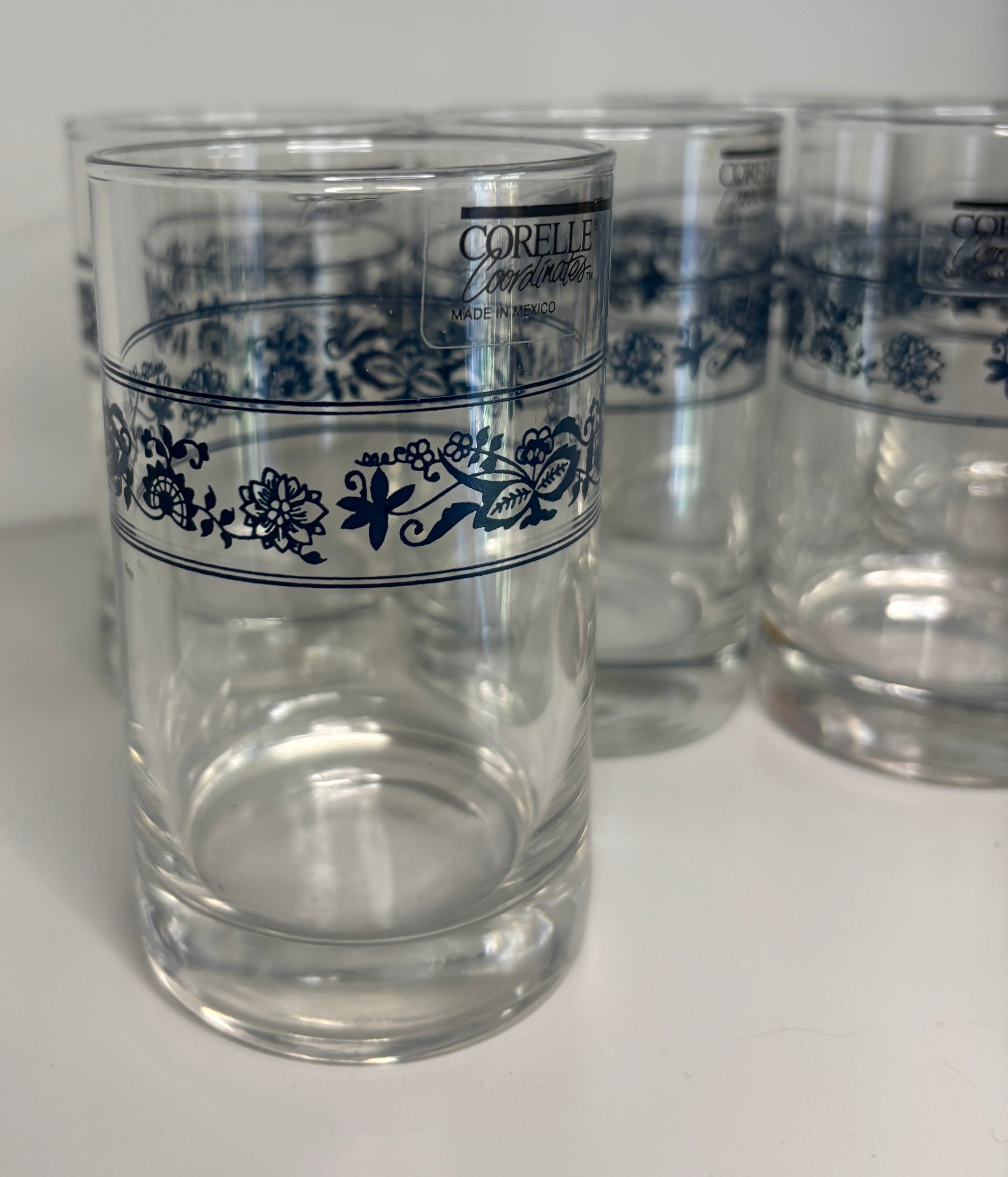 Clear glasses with blue floral patterns and Corelle branding on a white background