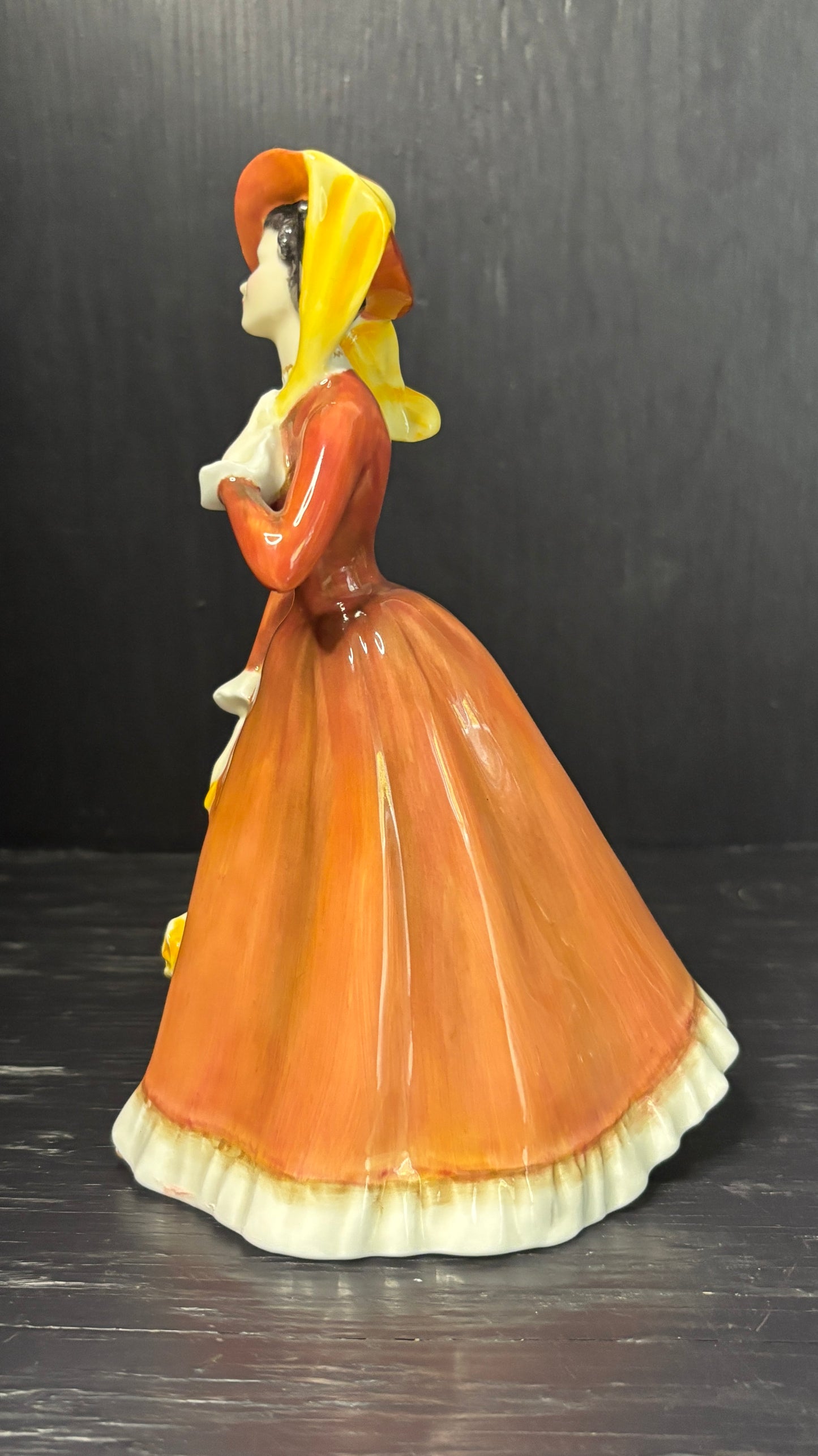 Figurine of a woman in an orange dress and yellow headscarf on a dark background