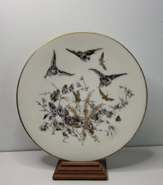 Decorative plate with bird and floral design on a stand against a plain background