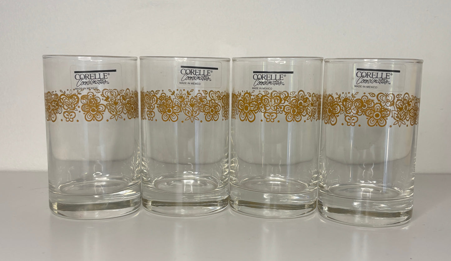 Four glass tumblers with gold decorative patterns and Corelle branding on a white background