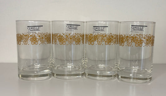 Four glass tumblers with gold decorative patterns and Corelle branding on a white background