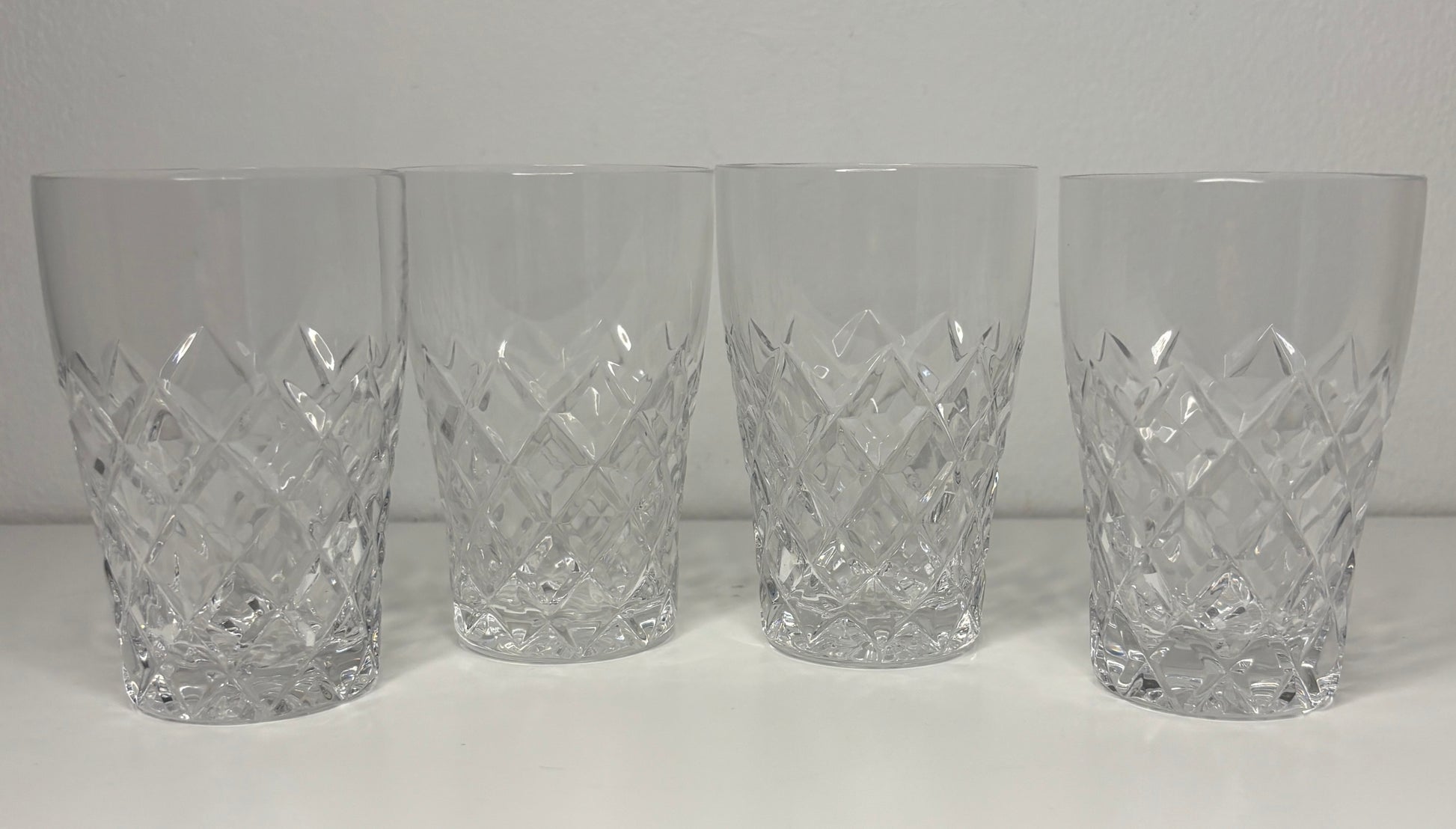 Four crystal tumblers with diamond cut pattern on a white background