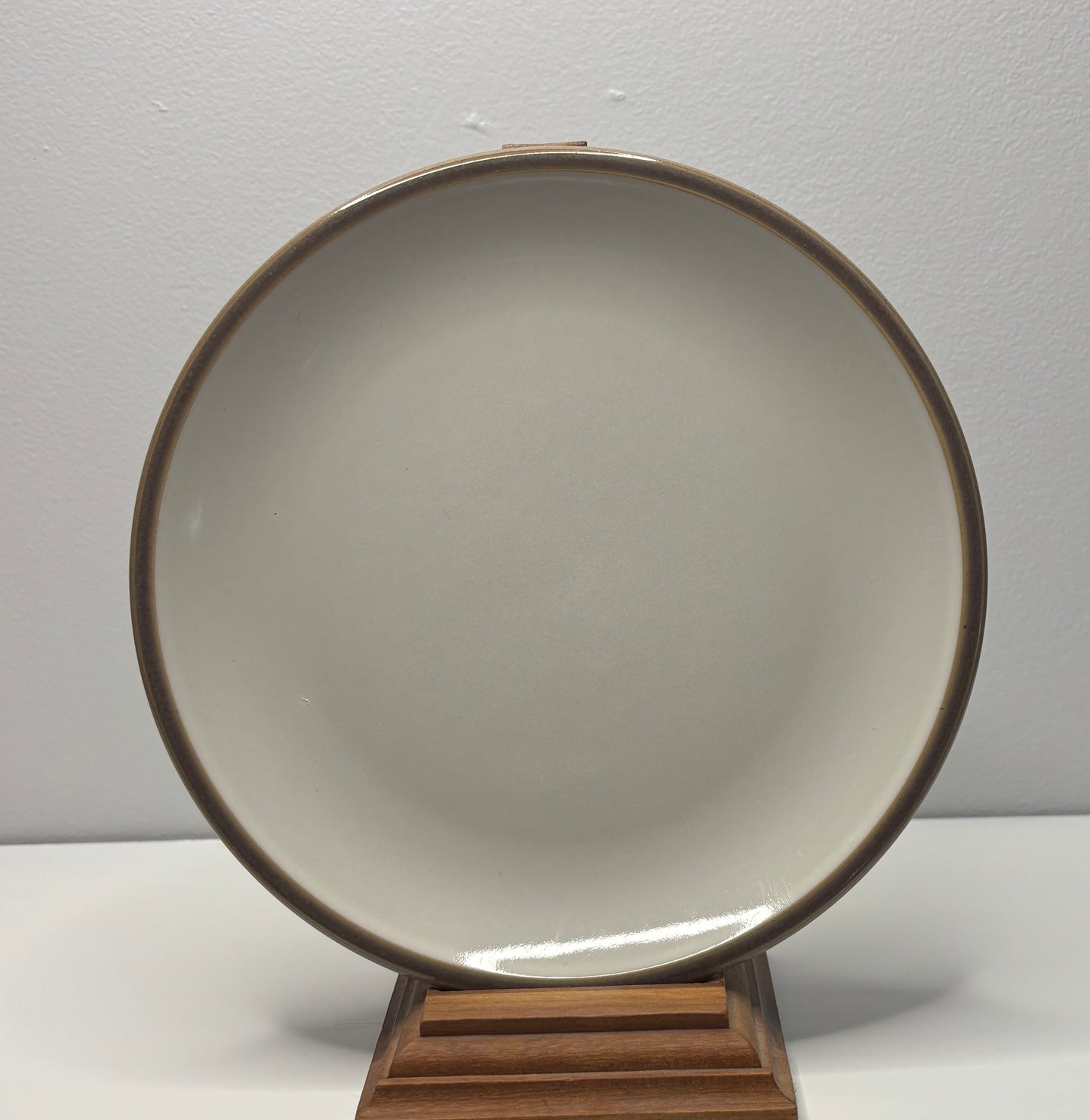 Round ceramic plate with brown rim on a wooden stand against a plain background