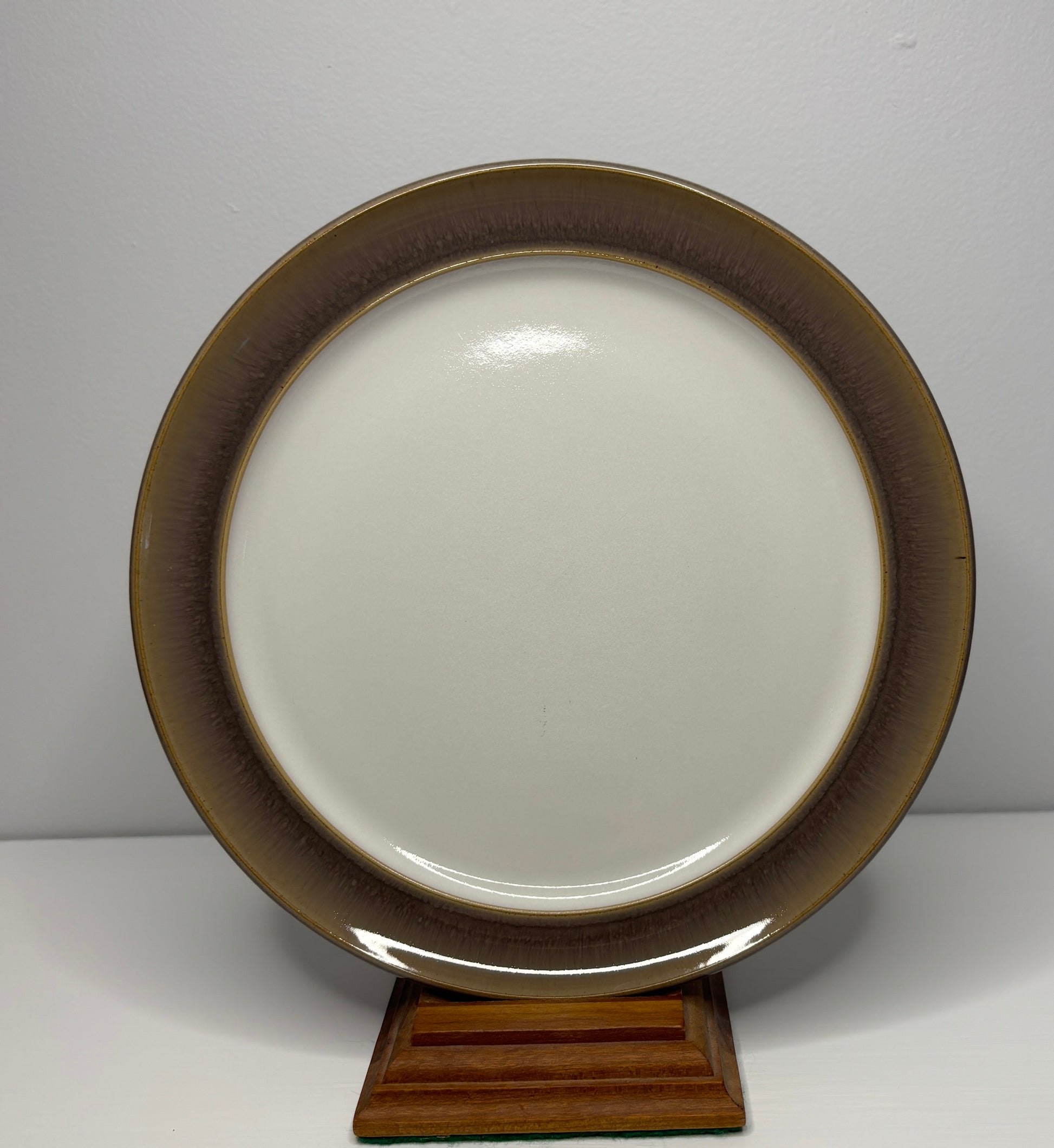 Ceramic plate with brown rim on a wooden stand against a white background