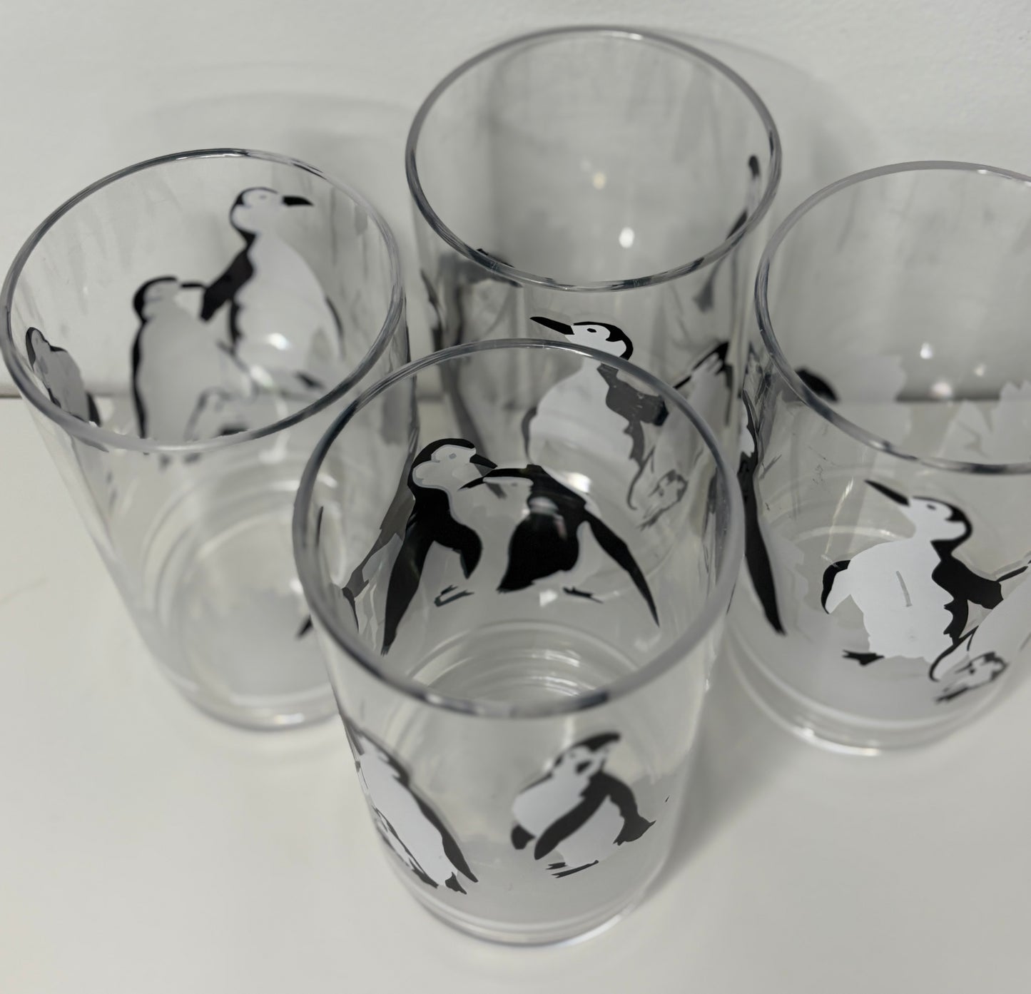 Four glass tumblers with penguin designs on a white background