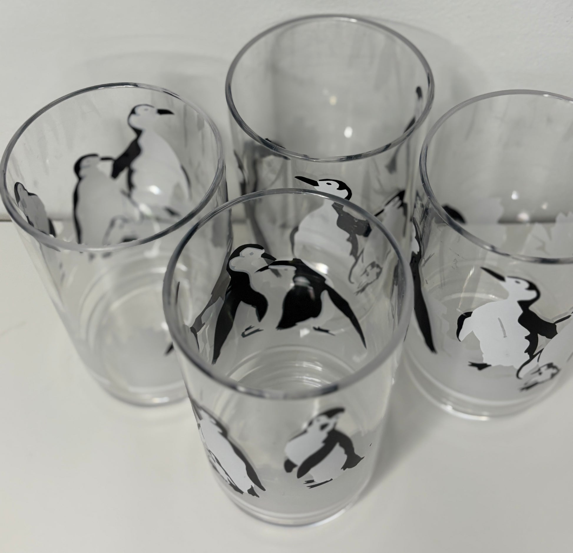 Four glass tumblers with penguin designs on a white background