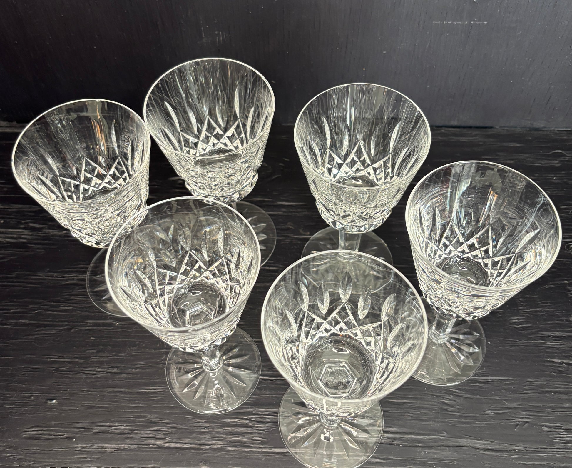 Set of six crystal glasses with cut patterns on a dark surface