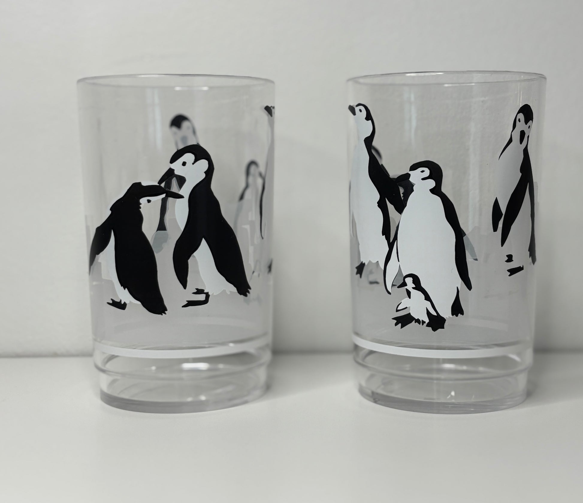 Two glass tumblers with black and white penguin illustrations on a white background