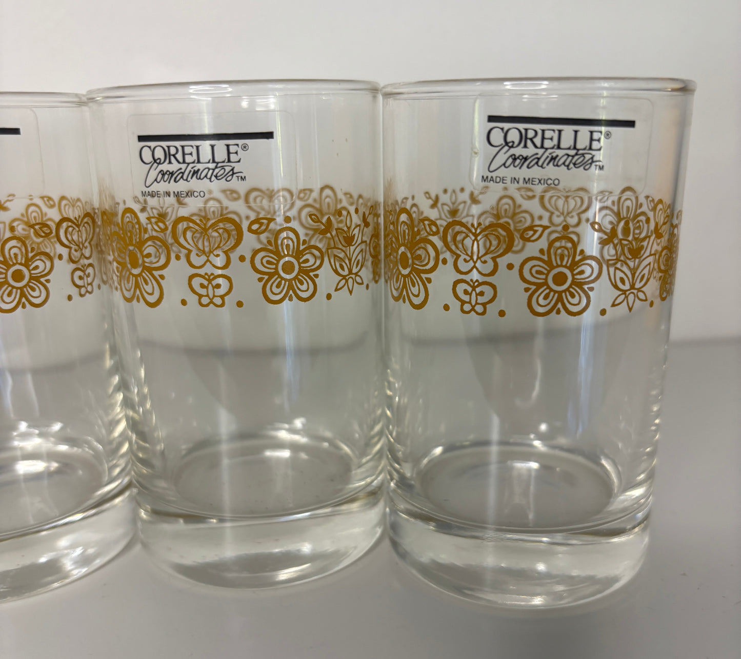 Three clear Corelle glasses with gold floral patterns on a white background