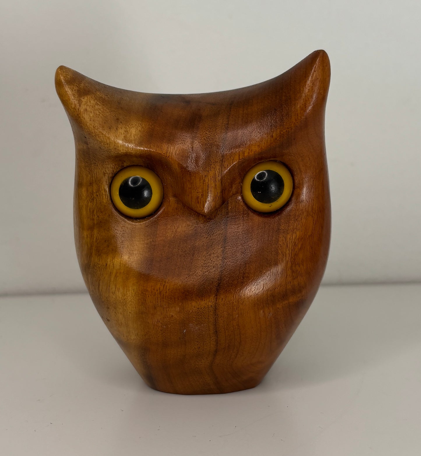 Wooden owl figurine with yellow eyes on a plain background