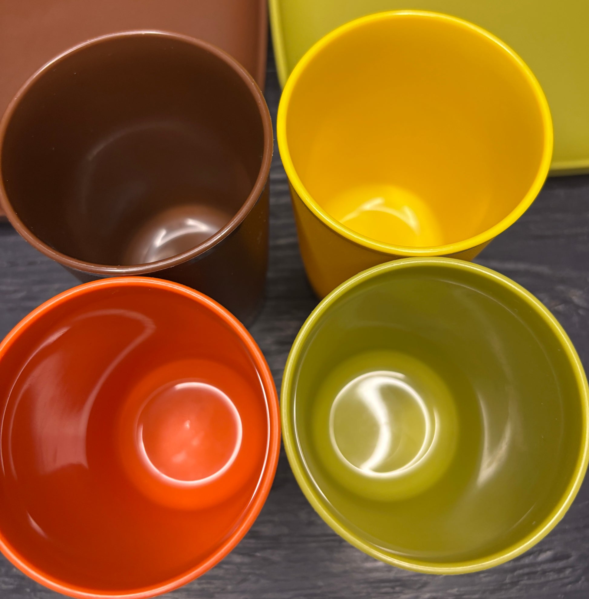 Four colorful ceramic bowls in brown, yellow, orange, and green on a dark surface.