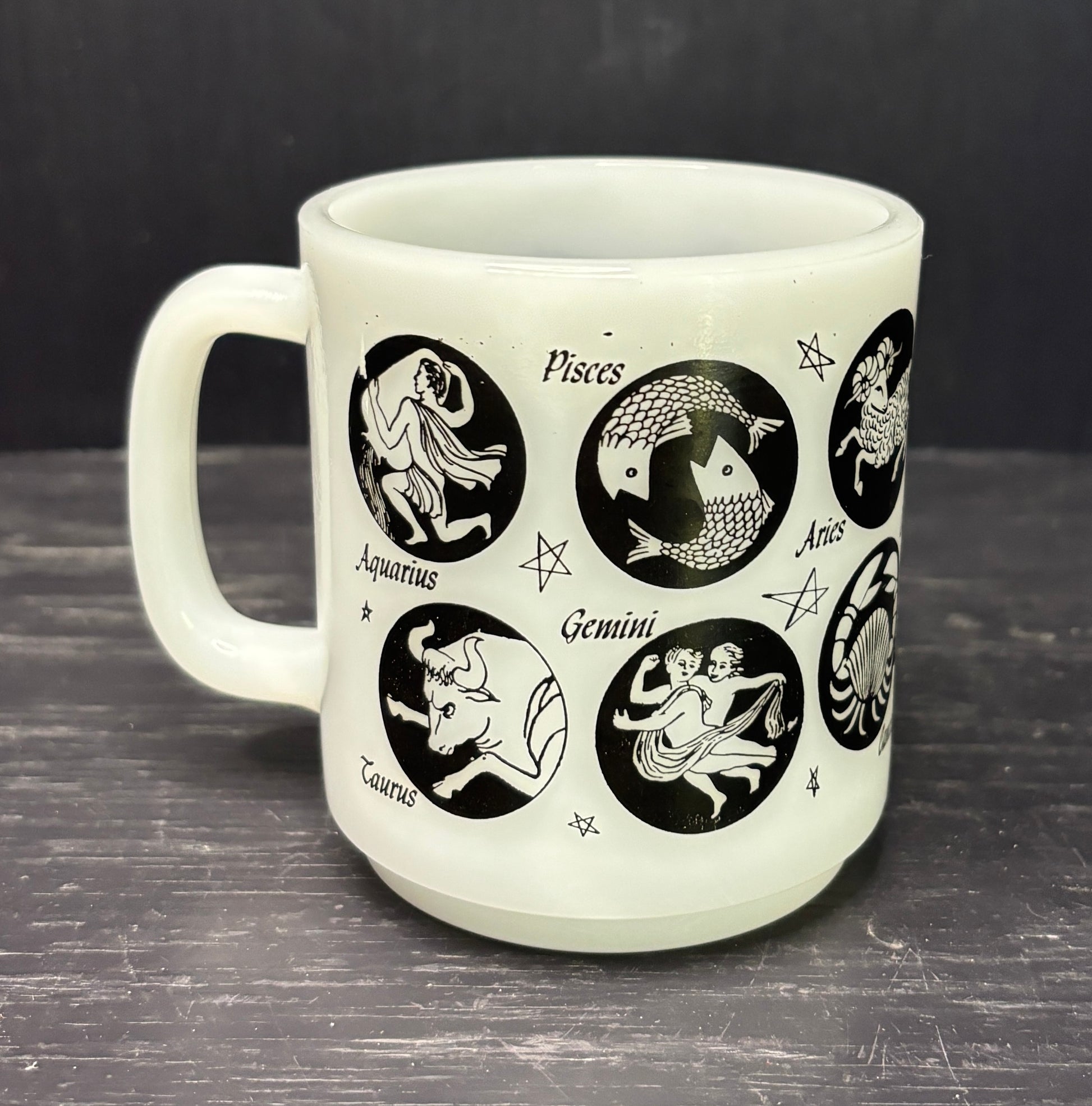 White mug with black astrological signs on a dark surface