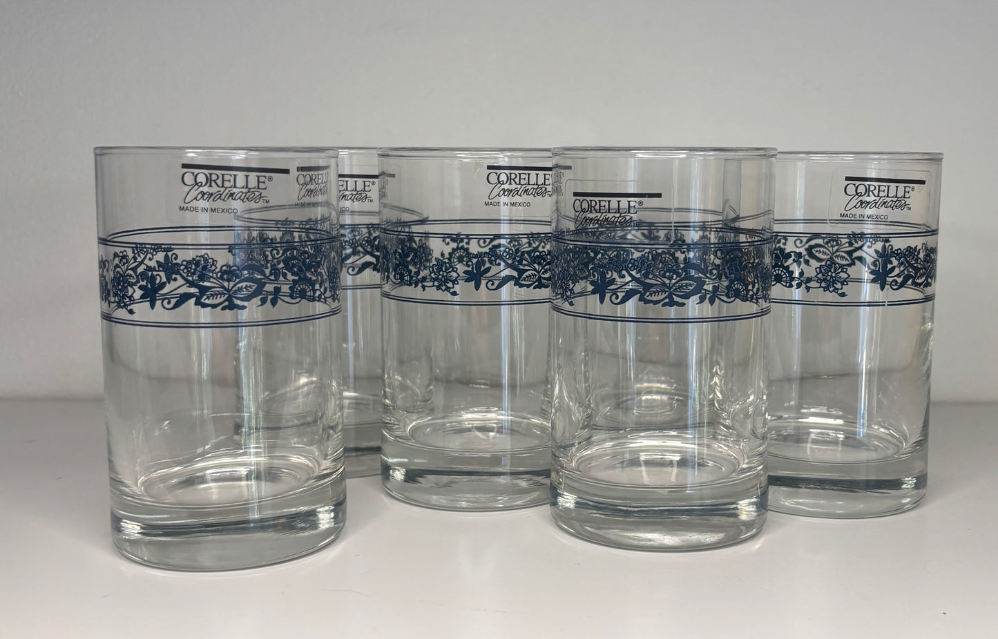Set of five Corelle glasses with blue floral patterns on a white background