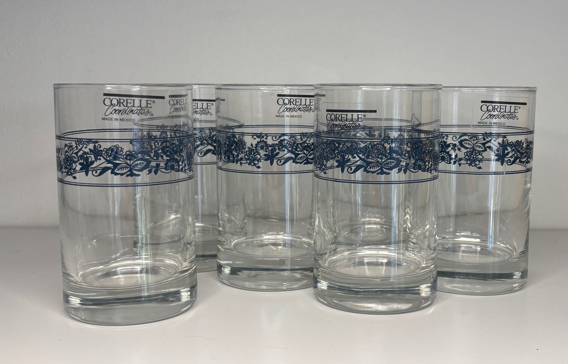Set of five Corelle glasses with blue floral patterns on a white background