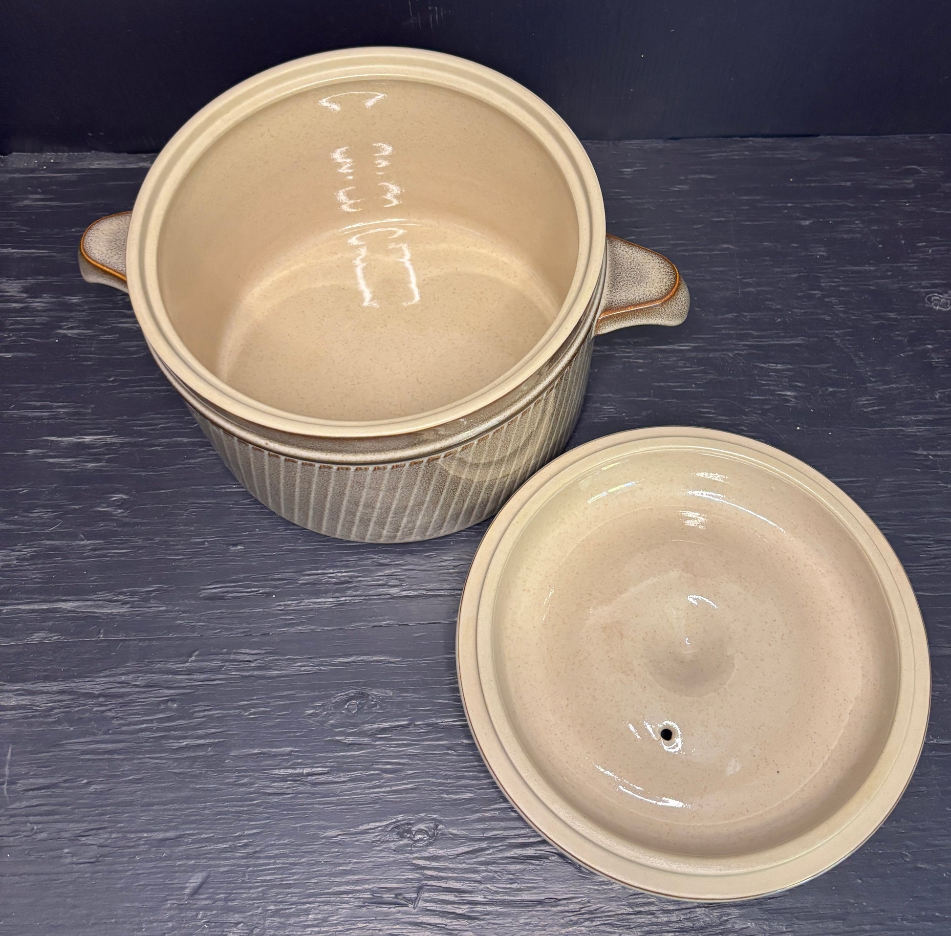 Two beige ceramic pots with lids on a dark wooden surface