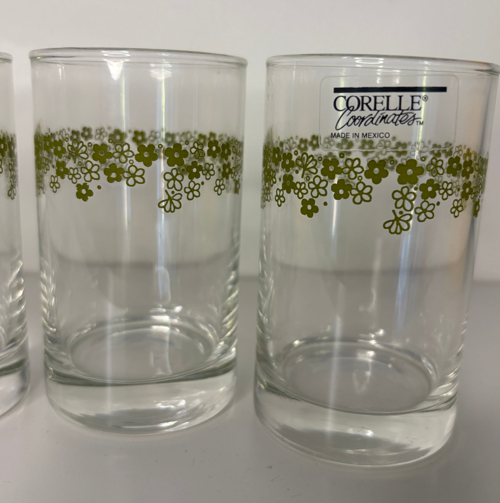 Clear glasses with green floral pattern and Corelle branding on a white background