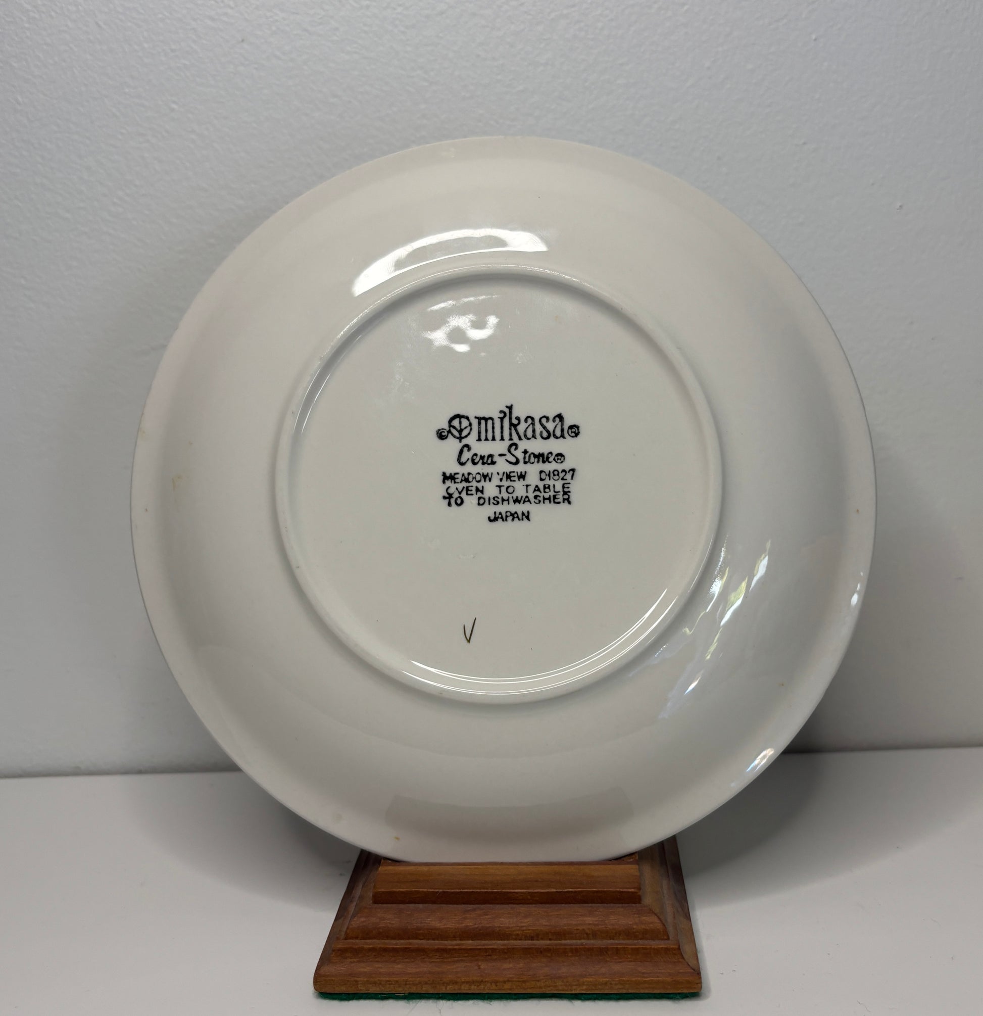 White ceramic plate with 'Amfikasa' branding on a wooden stand against a white background