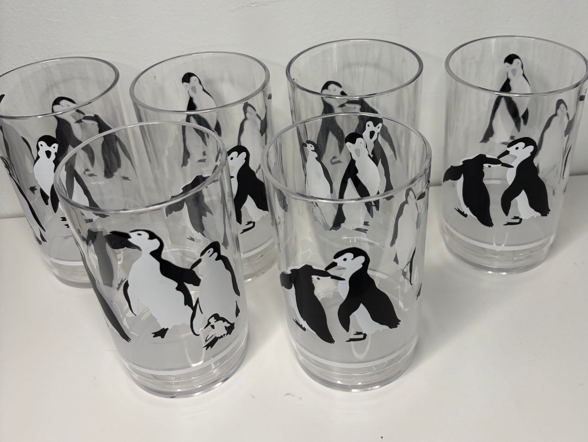 Set of six clear glasses with black and white penguin illustrations on a white background