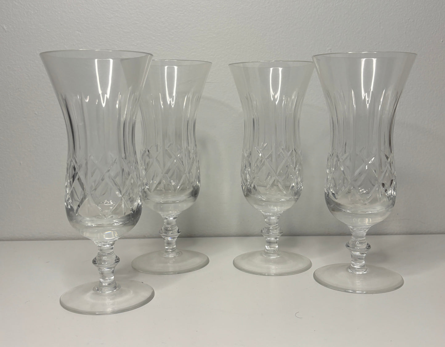 Four clear glass goblets with intricate designs on a white surface and gray background
