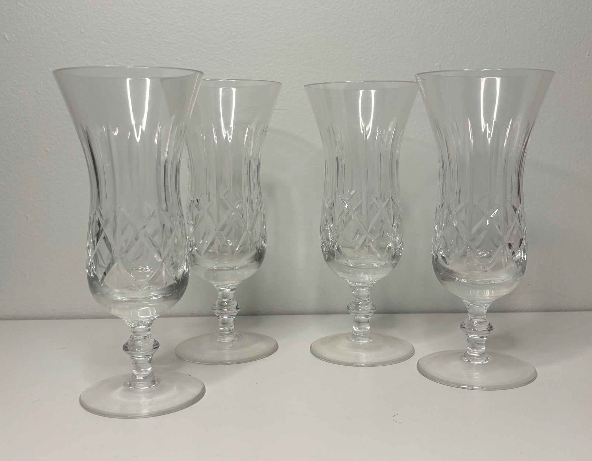 Four clear glass goblets with intricate designs on a white surface and gray background