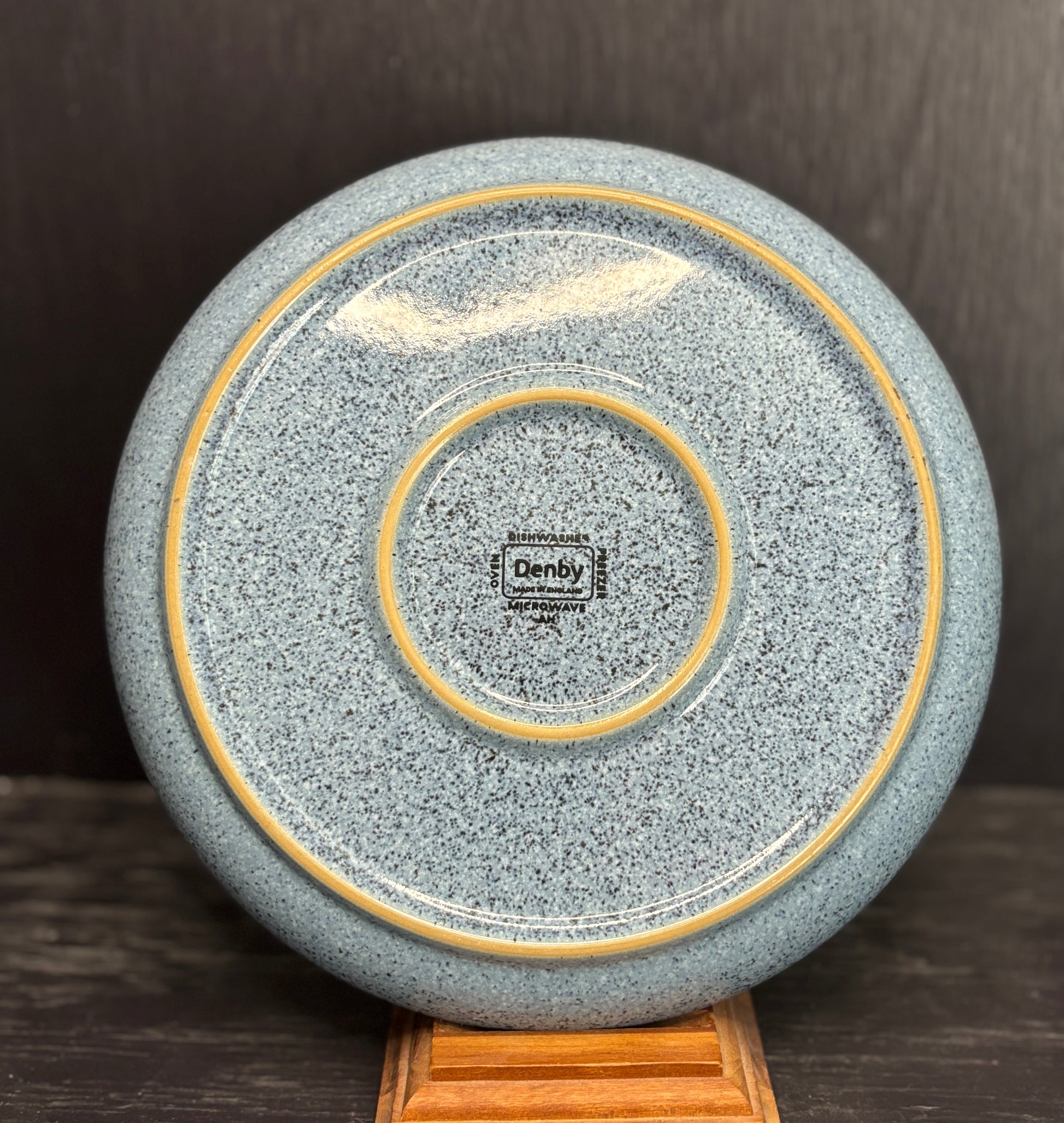 Speckled gray ceramic plate with gold rim on a wooden stand against a dark background