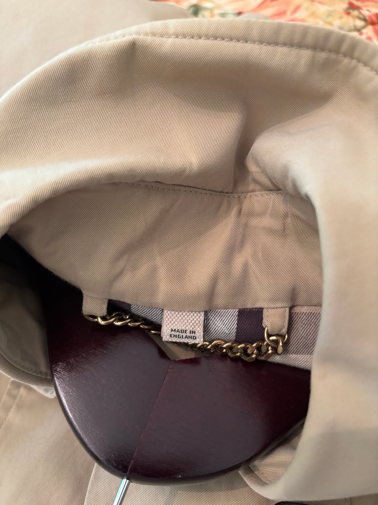 Close-up of a beige hat with plaid interior and gold chain detail.