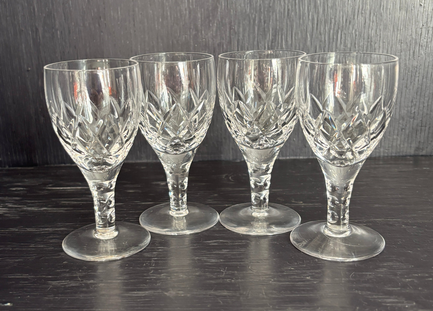 Set of four clear glass sherry glasses on a dark wooden surface