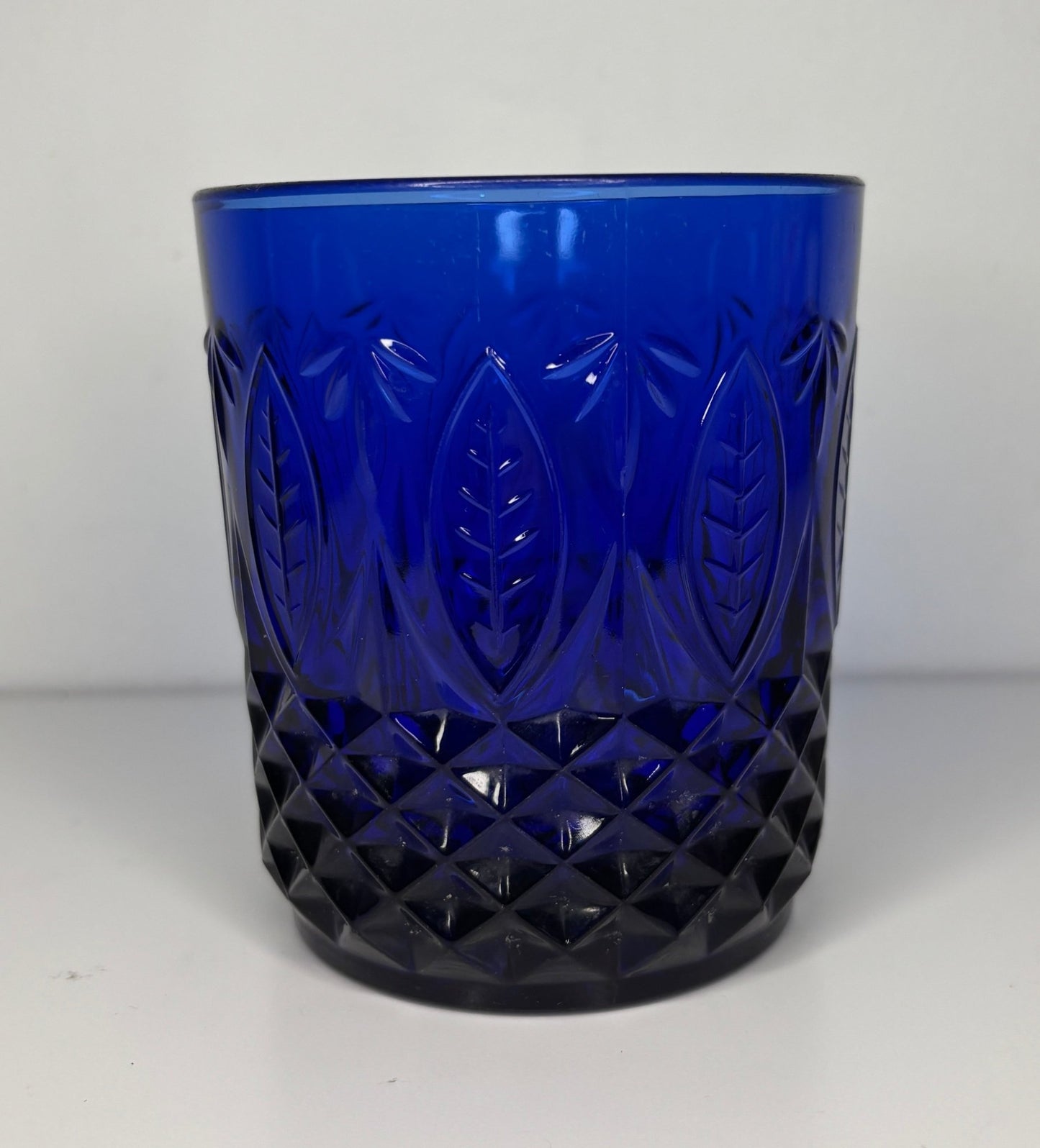Blue glass tumbler with diamond and leaf patterns on a white background