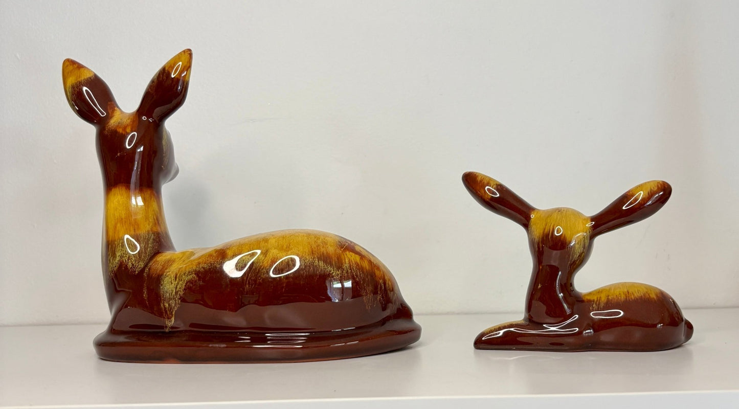 Two ceramic deer figurines on a white surface with a plain background