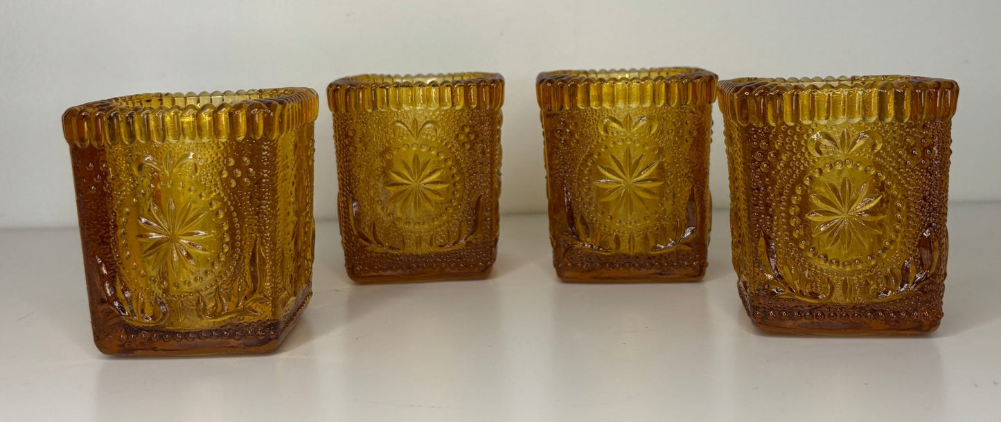 Four gold-colored glass candle holders with embossed designs on a white background
